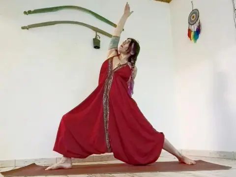 Woman in flowing red bohemian dress practicing yoga in a bright, peaceful room with dreamcatcher decor.