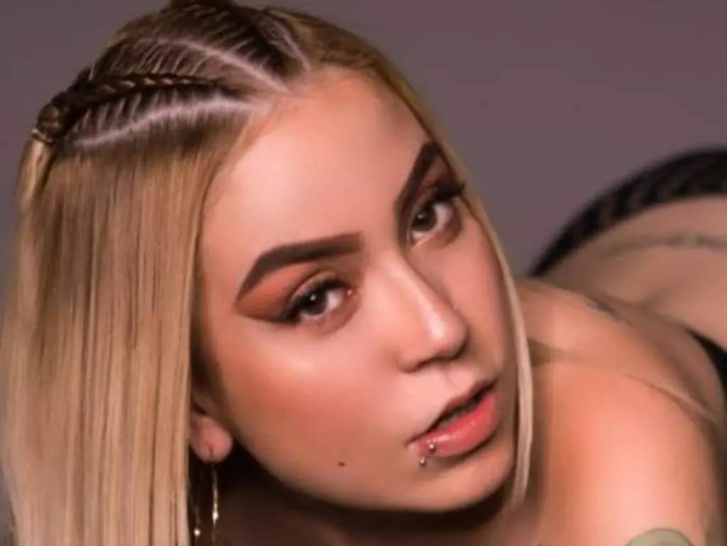 SaraCrush looks into the camera with blonde hair and a lip piercing while posing in a close-up shot.