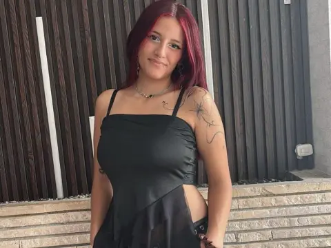 LiilyMoonn smiles in a black tank top while showing off her red hair and shoulder tattoos.