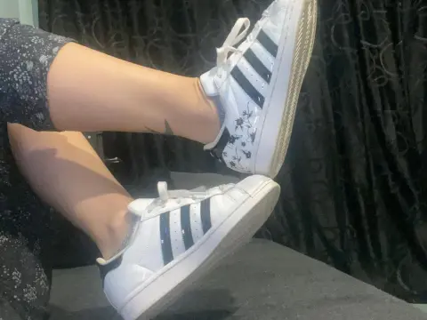 MistressBB — Woman in floral patterned leggings wearing white Adidas Superstar sneakers in a cozy indoor setting.