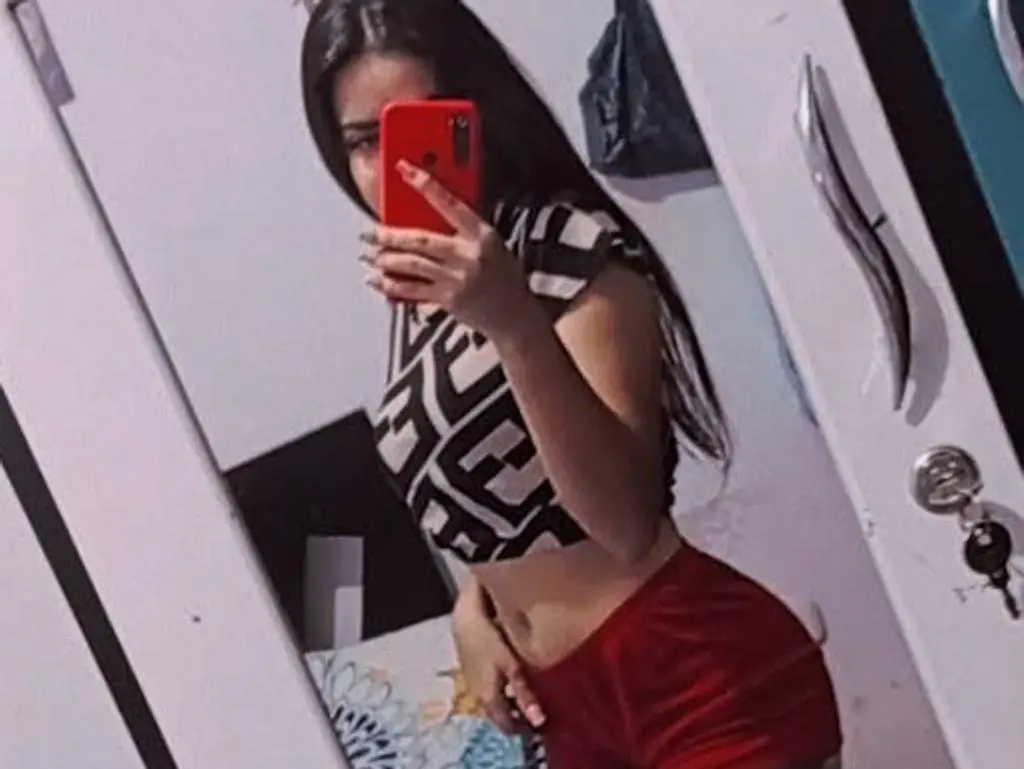 HotCharlotte takes a mirror selfie wearing a black and white patterned crop top and red shorts.