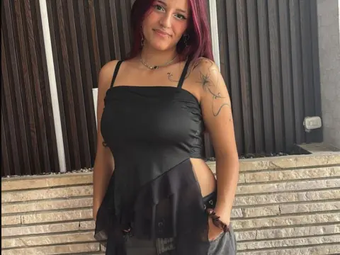 LiilyMoonn poses outdoors in a black tank top and grey shorts, showing off her red hair and tattoos.
