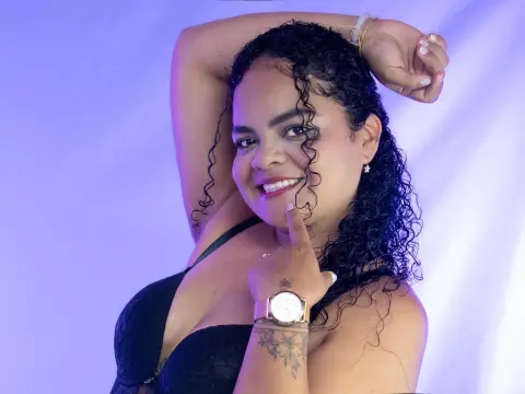 LenaRushss poses with one arm raised, wearing a black lace bra and showing her curly dark hair and gold watch against a purple background.