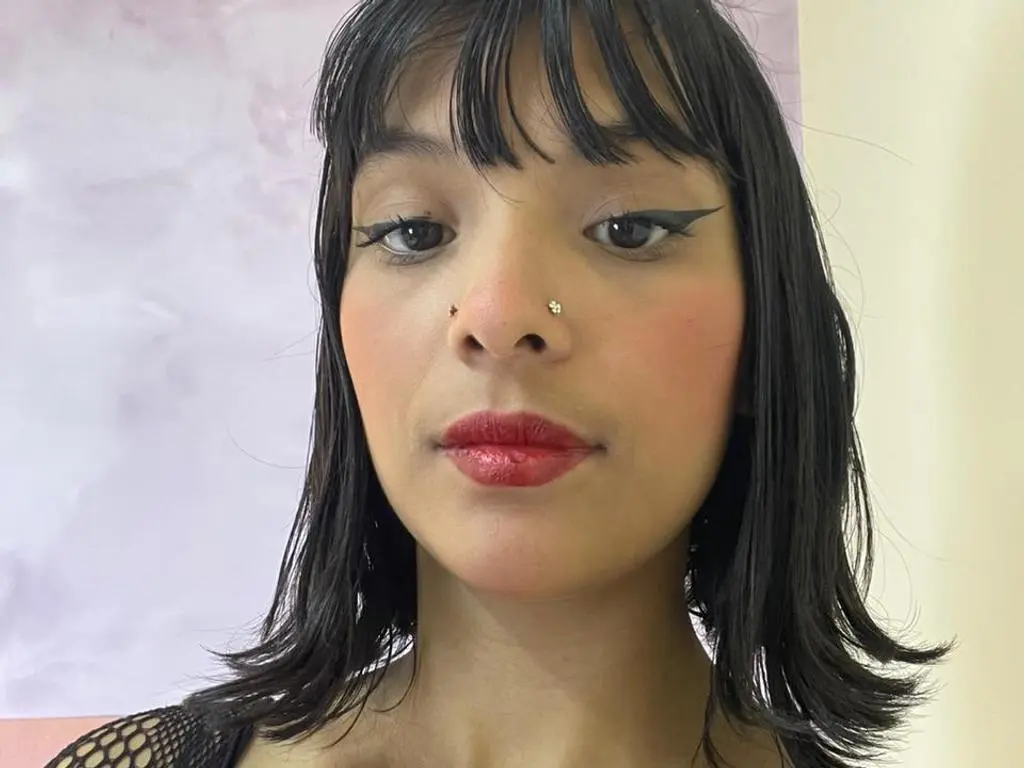 CHELIMAMLDONADO looks directly at the camera with dark hair, winged eyeliner, and red lipstick against a light background.