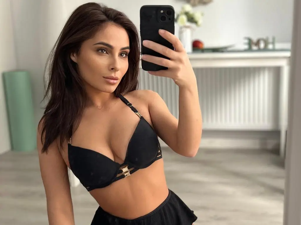 SarahSkye895 poses for a mirror selfie wearing a black bra and skirt, showing off her long dark hair and cleavage.