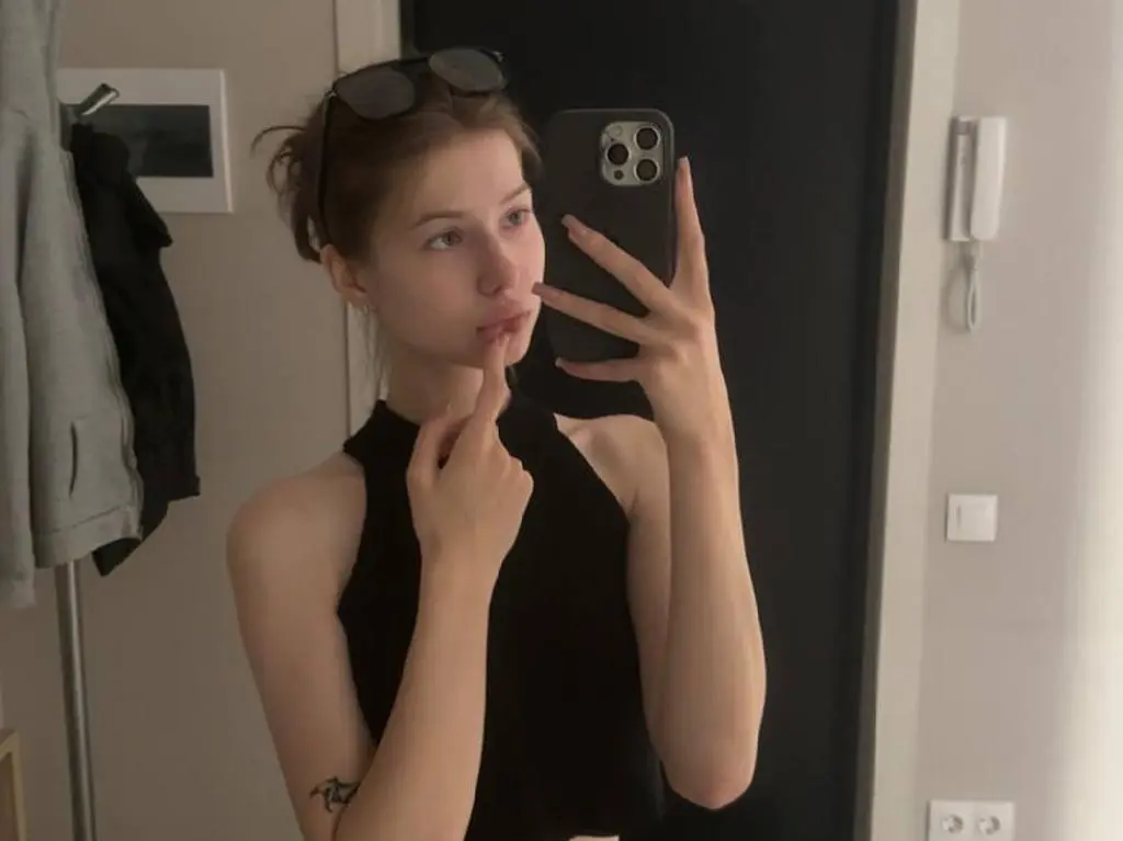 Milllie — Milllie takes a mirror selfie wearing a black halter top, looking at the camera while touching her lip with one finger.