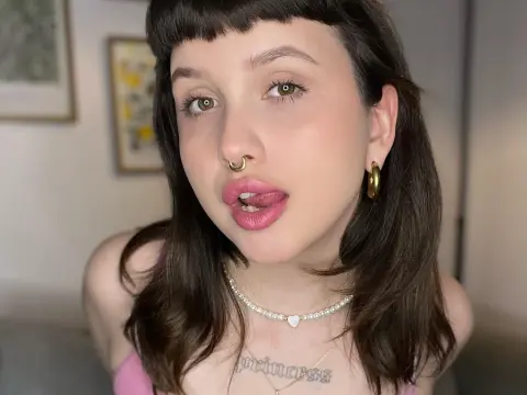 hellfirekiss_ — hellfirekiss_ shows her face and neck, wearing a pearl choker and gold hoop earrings, with her tongue poking out past her pink lips.