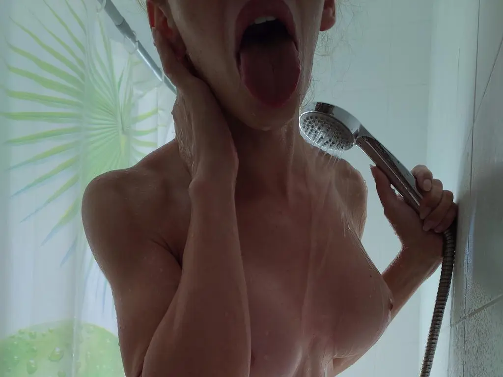 angelmouth1 is naked in the shower with her mouth wide open and tongue out while holding a shower head.
