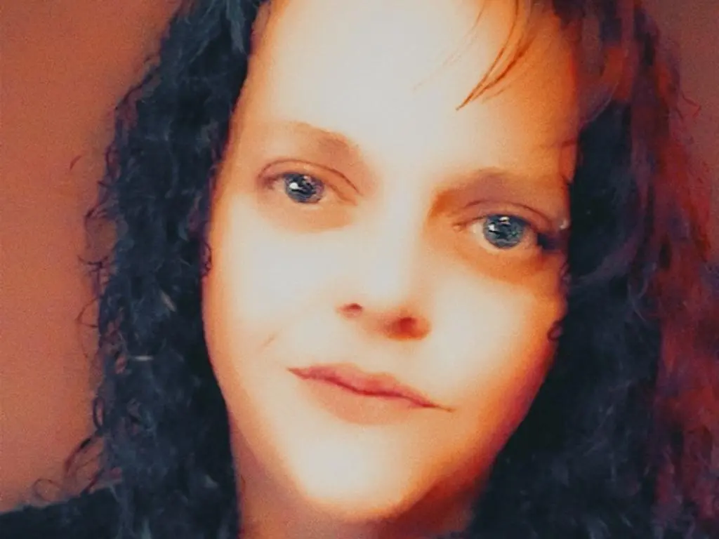 TinyDoll looks directly at the camera with her long, dark curly hair framing her face.