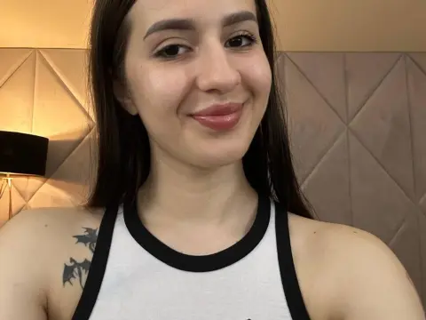 AlesiaDesmond smiles while wearing a white tank top with black trim, showing her long dark hair and shoulder tattoo.