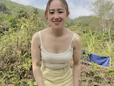Layla84 — Layla84 smiles in a white tank top and yellow skirt while posing outdoors in a lush, green field.