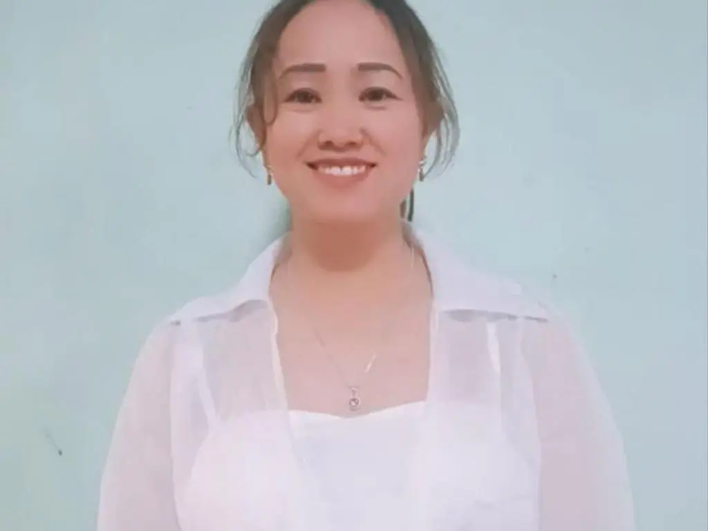 Layla84 is a smiling woman with dark hair wearing a white sheer blouse and a necklace against a light blue background.