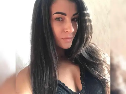 Karinabrunette — Karinabrunette poses with her long dark hair down, wearing a black lace top or bra against a light background.