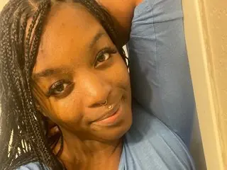 69blackbarbie smiles while looking at the camera, showing her face and dark hair in a close-up shot.