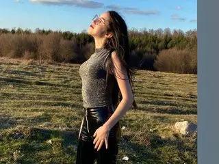 ADIYNE poses in a field at sunset, wearing a grey sleeveless top and black leather pants, looking up with her long dark hair down.
