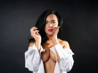 Glamorous woman with long dark hair in an open white shirt posing against a black background.