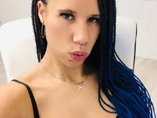 AaliyahHarris poses close-up, looking at the camera with her dark hair in long braids and wearing a black strap top.