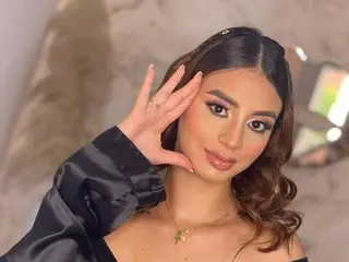 AbbyChannel poses with her hand against her face, showing her long brown hair and light makeup in a close-up shot.