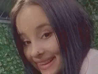 AdelineRosa smiles closely at the camera, showing her face and dark hair against a leafy green background.
