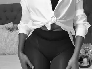 Africanblackdoll99 poses in a white button-down shirt tied at the waist, showing her midriff and dark skin in a black and white photo.