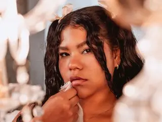 Young woman with wavy dark hair and gold hoop earrings posing with a dreamy, soft-focus aesthetic.