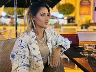 Stylish woman in a tie-dye jacket sitting at an outdoor cafe table during a warm evening.