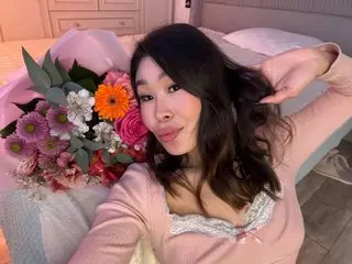 Smiling woman in a pink lace top relaxing in bed with a large colorful bouquet of flowers.