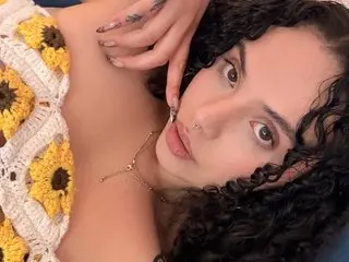 AlanaBianco with curly dark hair poses closely to the camera wearing a white and yellow sunflower crochet top.
