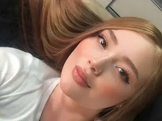 Alana_Velvet poses with her long, light brown hair spread out, wearing a white top and looking directly at the camera.