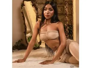 AlannaKristen poses nakedly in a tan bra and matching bottoms, showing her cleavage and curves against a warm, golden background.