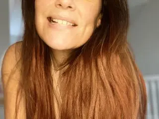 AleishaKay smiles with her long brown hair down, showing her face and bare shoulders against a soft, bright background.