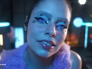 Woman with futuristic blue eye makeup and glitter in a neon-lit cyberpunk setting.