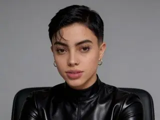 Alessandrademons looks directly at the camera with short black hair, wearing a black leather top against a plain grey background.