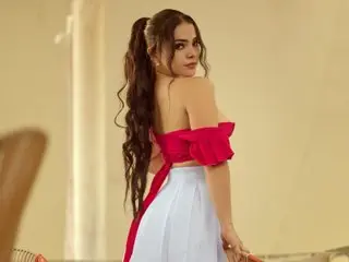 AlessiaRou poses looking over her shoulder, wearing a red strapless top and white skirt with her long dark hair flowing down her back.