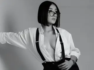 Alesxia poses in a white button-down shirt, left open to show her bare breasts, paired with black suspenders and dark hair in a bob cut.