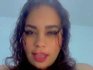 AlexxandraRivera poses with wet, wavy dark hair and a direct gaze, showing her face and shoulders against a plain light background.