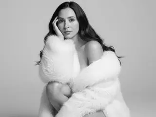AliCoper poses with her hands framing her face, showing her long dark hair and bare shoulders against a plain light background.