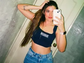 AlicceGray poses for a mirror selfie wearing a black tank top and denim shorts, running her hand through her long brown hair.