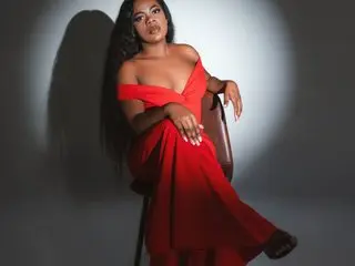 Elegant Black woman in a flowing red off-the-shoulder gown sitting gracefully in a studio setting.