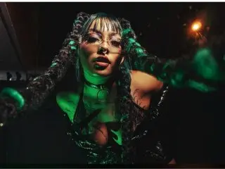 AliceWalter poses with long bangs and glasses, wearing a black choker and dark lace outfit against a dark background.