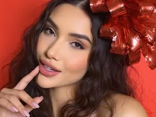 Alice_Haaze poses close-up with long wavy dark hair and soft makeup against a red background.