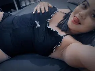 Young woman in a black ribbed camisole relaxing on a bed with a playful expression.