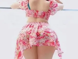 Woman in a pink floral print crop top and matching mini skirt posing in a bright summer setting.