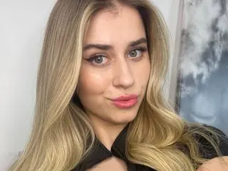 Blonde woman in a black top with soft makeup posing in a bright indoor setting.