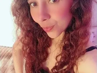 AlisonAndreeD poses with her long, curly red hair framing her face in a close-up shot wearing a black top.
