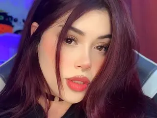 Alisson_Velt poses with a close-up headshot, showing her long dark hair and red lips against a soft purple background.
