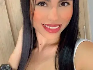 Alissonbeltran smiles with her long black hair down, wearing a white tank top top in a close-up headshot.