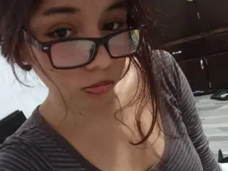 AllicePetit looks at the camera with long brown hair, wearing a grey long-sleeved shirt in a close-up shot.
