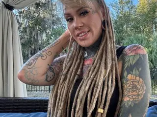 Altgirl88 smiles while leaning forward, showing her long blonde dreadlocks and colorful arm tattoos.
