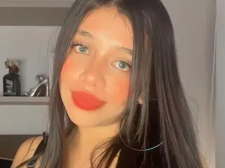 Aly_Eve poses for a close-up selfie, showing her face, long dark hair, and light makeup against a neutral indoor background.